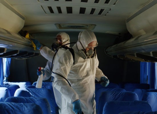 HazMat team in protective suits decontaminating public transport tourist bus interior during virus outbreak