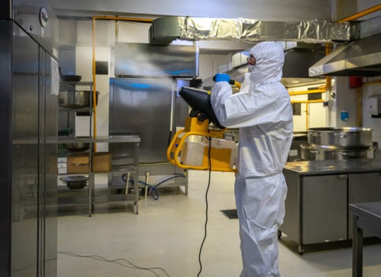 man in protective equipment disinfects with a spray gun industrial kitchen surfaces due to coronavirus covid-19 .Virus pandemic