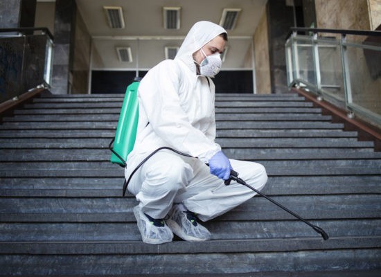 Shot of male person in white chemical protection suit disinfecting public corridors and steps to stop spreading highly contagious corona virus. Stop coronavirus or COVID-19.